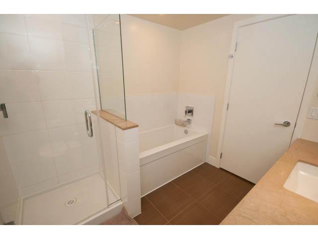 Spacious bathroom with modern fixtures, glass shower, and wooden vanity. - 1606-158 West 13th Street, North Vancouver