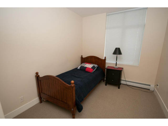 Furnished bedroom with wooden bed, dark bedding, and sliding blinds. - 1606-158 West 13th Street, North Vancouver