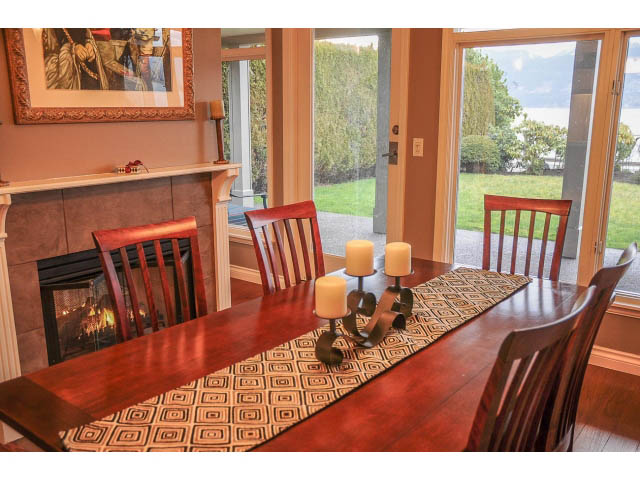 Dining area with wooden table, chairs, and fireplace, leading to a garden view. - 3199 Pt. Grey Road, Vancouver West Side