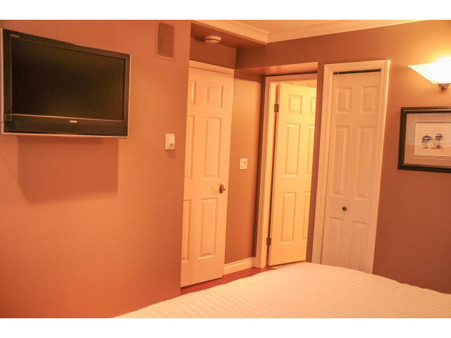 Furnished bedroom with a flat-screen TV, open closet doors, and a bed with striped bedding. - 3199 Pt. Grey Road, Vancouver West Side