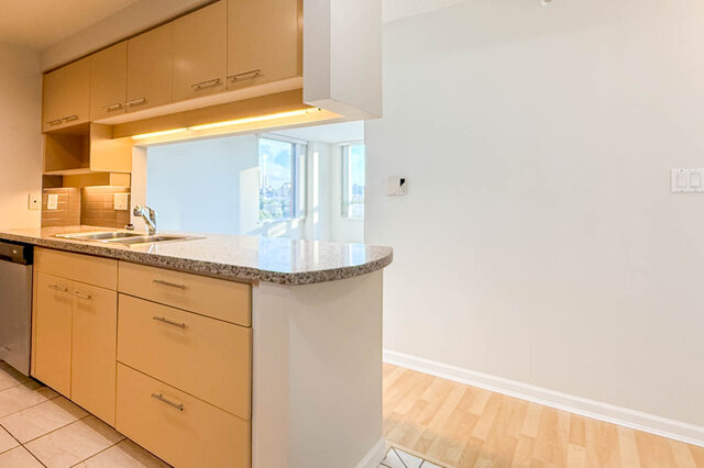 The kitchen's granite peninsula with a double sink under the cabinets, open to a bright window - 15B-199 Drake Street, Vancouver Downtown