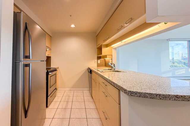 The galley kitchen with a stainless fridge and range, a long granite counter and a pass-through to the living room windows