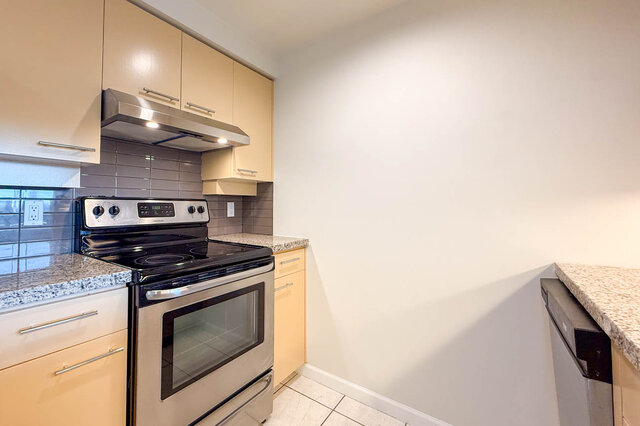 The stainless range under a hood, with a grey glass tile backsplash and granite counters - 15B-199 Drake Street, Vancouver Downtown