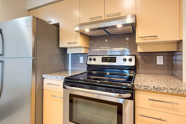 The stainless fridge and range with a grey glass tile backsplash - 15B-199 Drake Street, Vancouver Downtown