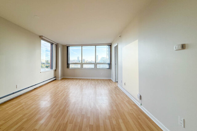 The long living room with corner windows looking out to the city and a glimpse of the water, on hardwood floors