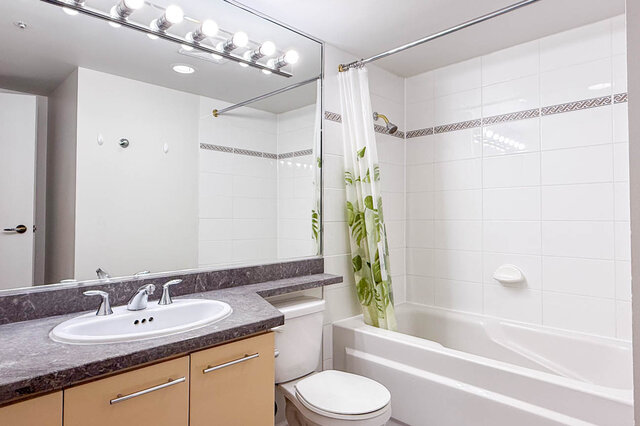 The main bathroom with a tub and shower, a long vanity and a large mirror with bulb lights - 15B-199 Drake Street, Vancouver Downtown