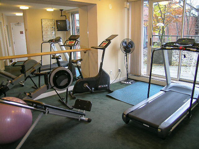 The building's shared gym with a treadmill, a bike and a rower beside a patio door - 15B-199 Drake Street, Vancouver Downtown