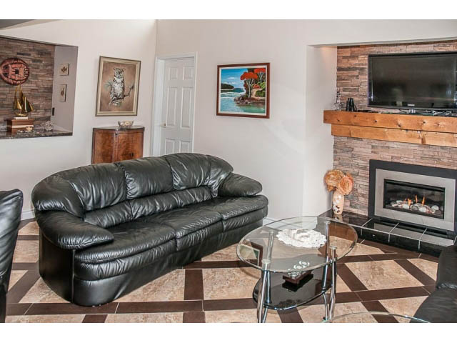 Living room with black leather couch, glass coffee table, and stone fireplace. - 4541 Strathcona Road, North Vancouver