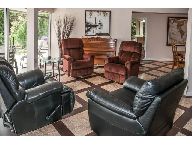 Living room with leather recliners and checkered floor, large windows, and piano in background. - 4541 Strathcona Road, North Vancouver