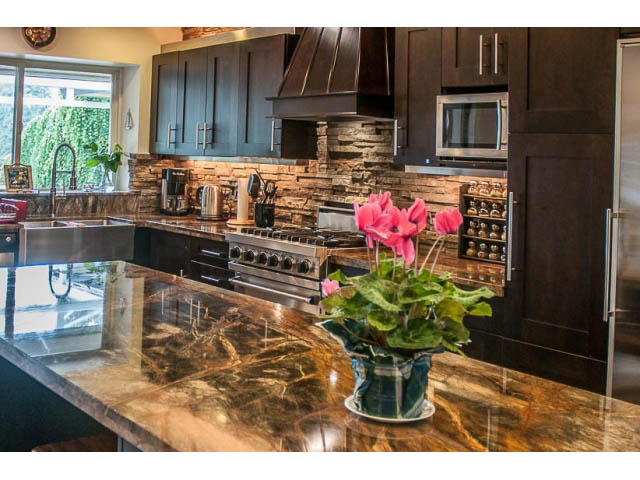 Bright kitchen with dark wood cabinets, granite countertops, and a stone backsplash. - 4541 Strathcona Road, North Vancouver