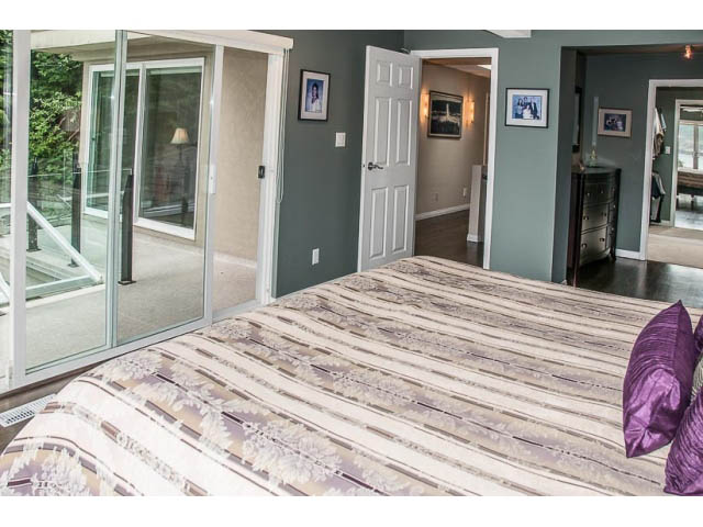 Furnished bedroom with striped bedding and sliding glass door leading to patio. - 4541 Strathcona Road, North Vancouver