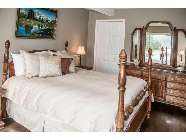 Spacious bedroom with wooden furniture, large bed, and scenic painting above. - 4541 Strathcona Road, North Vancouver