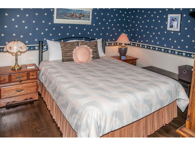 Furnished bedroom with star-patterned wallpaper, wooden nightstands, and a king-sized bed with a floral bedspread.