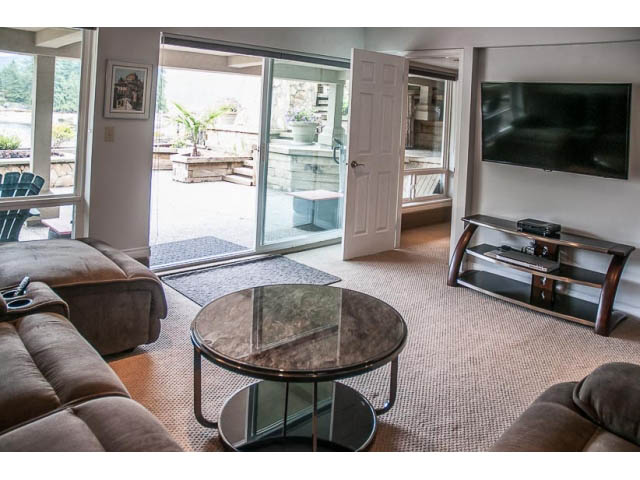 Spacious living room with modern furniture, large TV, and sliding glass door leading to patio. - 4541 Strathcona Road, North Vancouver