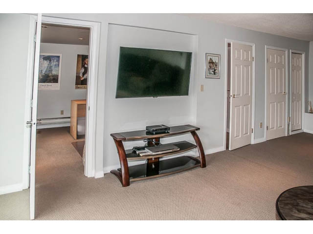 Living room with a flat-screen TV mounted on the wall, modern furniture, and carpeted floors. - 4541 Strathcona Road, North Vancouver