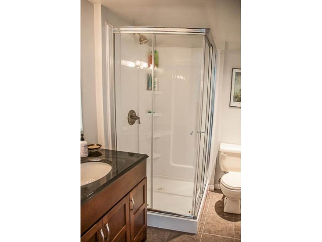 Bathroom with glass shower, wooden vanity, and toilet. - 4541 Strathcona Road, North Vancouver