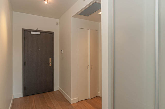 Furnished hallway with wooden floors and white walls, leading to a door. - 202 - 1409 W Pender St, Vancouver Downtown