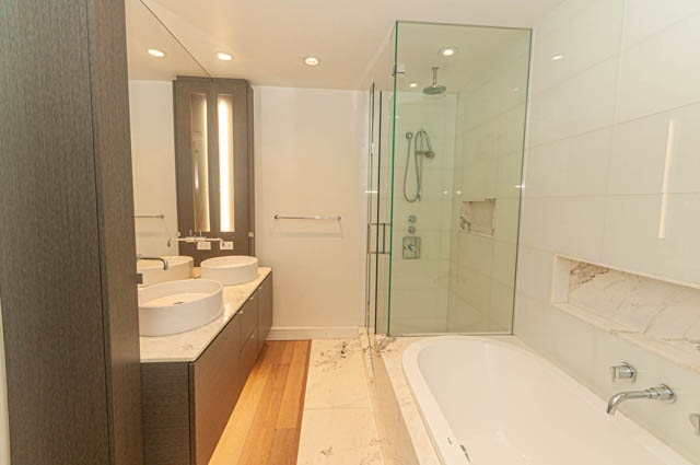 Furnished 1-bedroom + den with modern bathroom featuring glass shower, marble countertops, and hardwood floors.