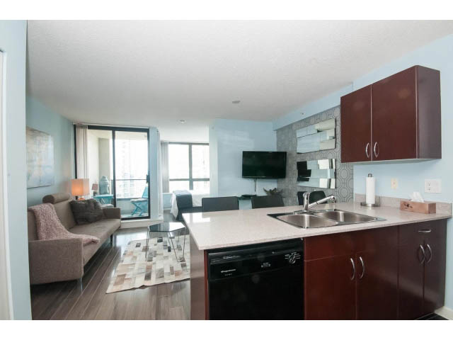 Bright kitchen with granite countertops and hardwood floors, leading to a cozy living area with a city view.