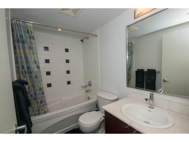 Bright bathroom with white countertop and modern sink, featuring a bathtub and shower with patterned curtain.