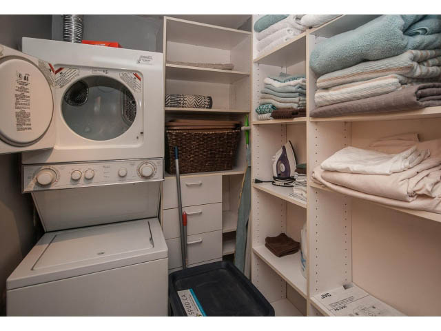 Compact laundry room with stacked washer and dryer, neatly organized shelves, and ironing board. - 3602 - 1111 W Pender, Vancouver Downtown
