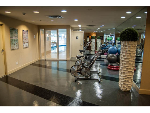 Spacious gym with exercise equipment and large windows, leading to a pool area. - 3602 - 1111 W Pender, Vancouver Downtown
