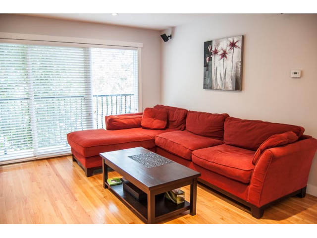 Furnished living room with red couches, hardwood floors, and large windows. - 2269 East 40th Ave, Vancouver East Side