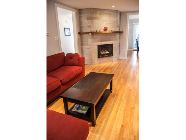 Living room with hardwood floors, red couch, and fireplace. - 2269 East 40th Ave, Vancouver East Side
