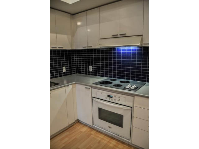 Bright kitchen with white cabinets, black tiled backsplash, and hardwood floors. - 138 Dunsmuir Street, Vancouver Downtown