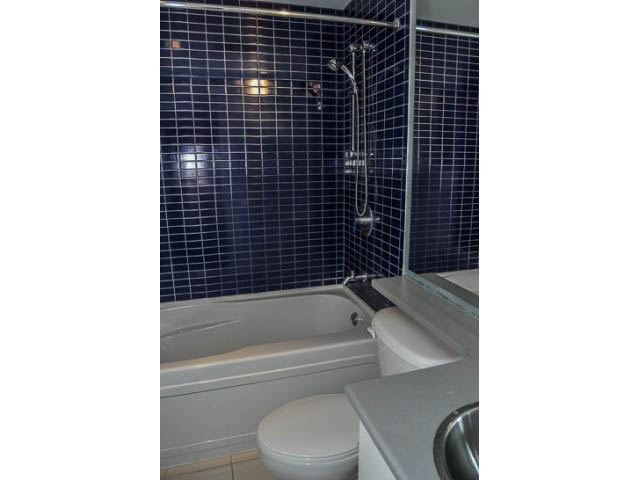 Furnished bathroom with dark blue tiles, white fixtures, and a bathtub. - 138 Dunsmuir Street, Vancouver Downtown
