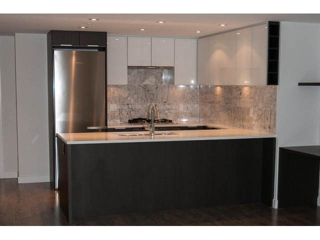 Modern kitchen with dark wood cabinets, marble backsplash, and stainless steel appliances. - 906 - 110 Switchmen St, Vancouver East Side