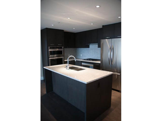 Modern kitchen with dark cabinets, stainless steel appliances, and white countertops. - 407-150 West 15th Street, North Vancouver