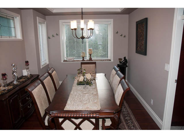 Formal dining room with dark wood furniture, chandelier, and window with blinds. - 4287 Madeley Rd, North Vancouver