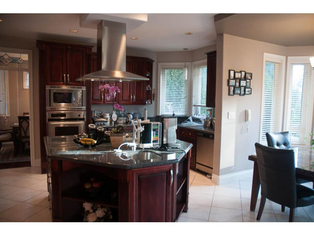 Bright kitchen with dark wood cabinets, stainless steel appliances, and a large island. - 4287 Madeley Rd, North Vancouver