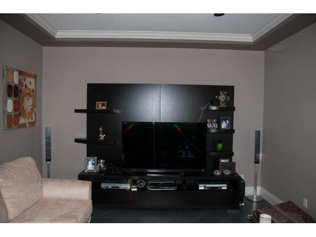 Living room with black entertainment center, modern decor, and a cozy beige armchair. - 4287 Madeley Rd, North Vancouver