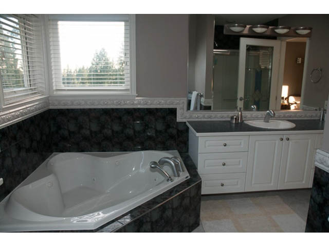 Spacious bathroom with marble countertops and a corner tub, city view through window. - 4287 Madeley Rd, North Vancouver