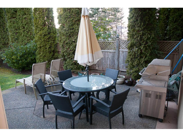 Furnished patio with outdoor furniture and umbrella, surrounded by greenery. - 4287 Madeley Rd, North Vancouver