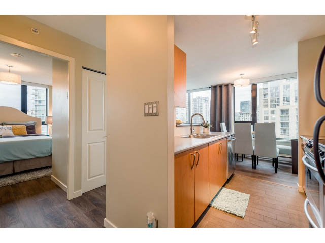 Bright kitchen with wooden cabinets and hardwood floors, leading to a cozy bedroom with a city view. - 1801 - 1295 Richards Street, Vancouver Downtown
