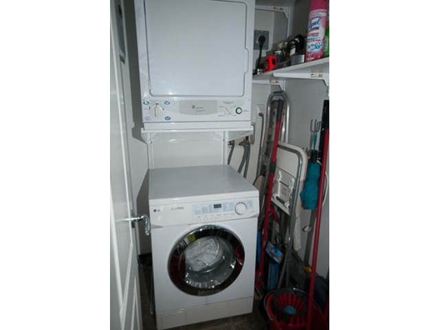 Bright laundry room with stacked washer and dryer, cluttered shelves, and cleaning supplies. - 705 - 1263 Barclay, Vancouver Downtown