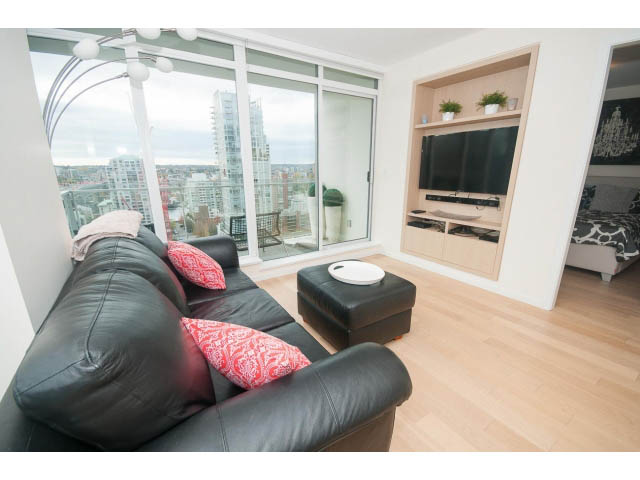 Bright living room with city view, black leather couch, hardwood floors, and built-in entertainment unit.