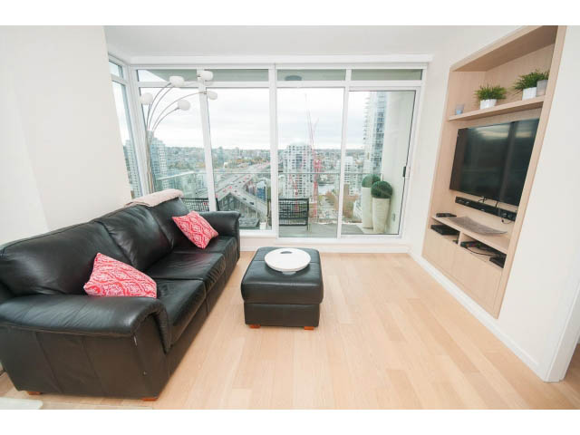Bright living room with hardwood floors, city view, and black leather furniture. - 1707 - 1351 Continental St, Vancouver Downtown