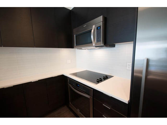 Bright kitchen with white countertops and dark cabinets, modern appliances, and hardwood floors. - 309 - 2665 Mountain Hwy, North Vancouver