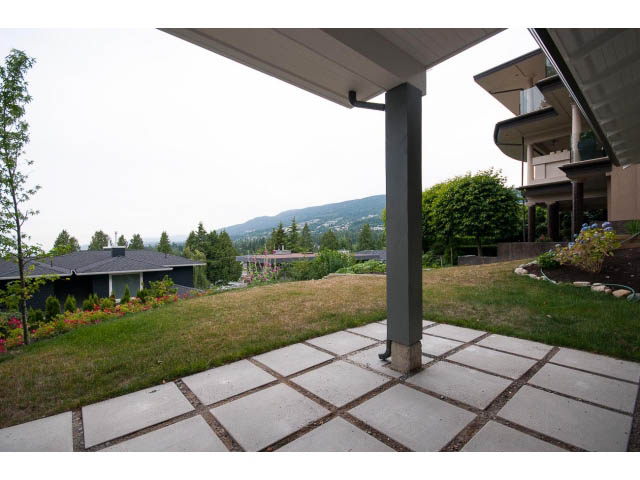 Furnished patio with grass, flowers, and distant mountain view. - 905 Braeside St, West Vancouver