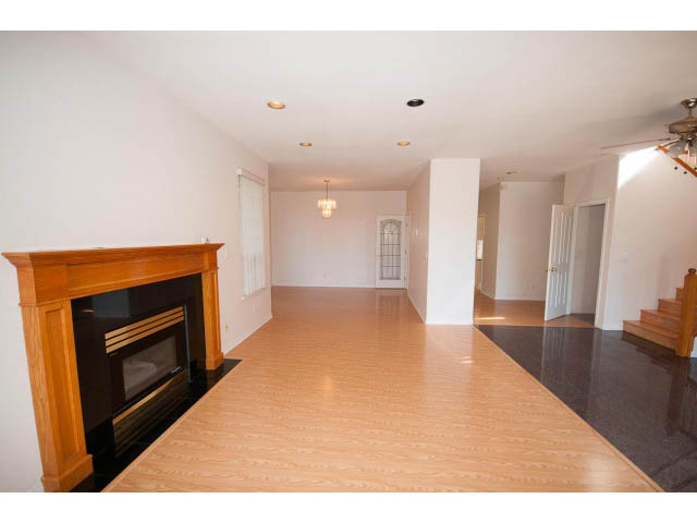 Open living space with hardwood floors and a fireplace, leading to a kitchen area. - 1559 Mathers Ave, West Vancouver