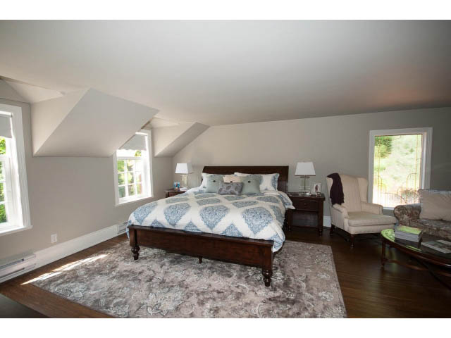 Spacious attic bedroom with sloped ceiling, large windows, and a cozy bed setup. - 3364 Redfern Pl., North Vancouver