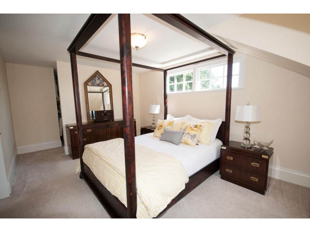 Spacious 4-bedroom + den, furnished attic bedroom with wooden four-poster bed, large windows, and carpeted floors. - 3364 Redfern Pl., North Vancouver