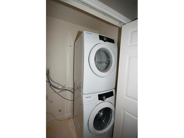 Laundry room with stacked washer and dryer, clean white walls, and a door. - 3 - 260 East 4th St, North Vancouver