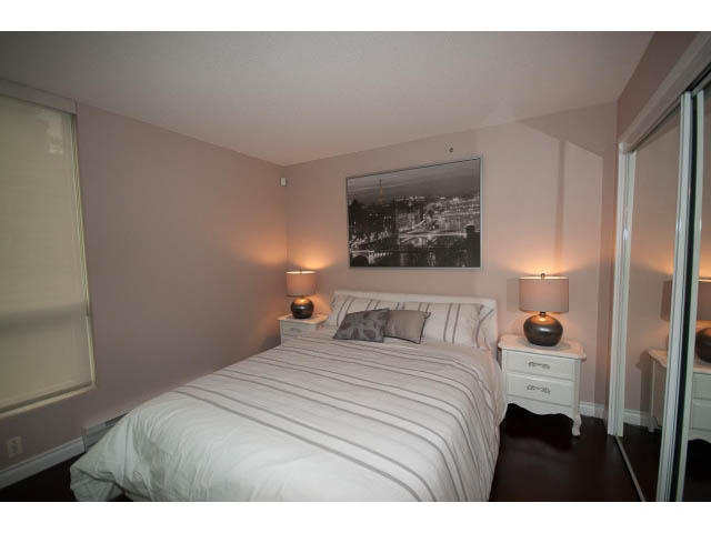 Furnished bedroom with striped bedding and a large window, showcasing a cityscape. - 502 - 555 Jervis, Vancouver Downtown