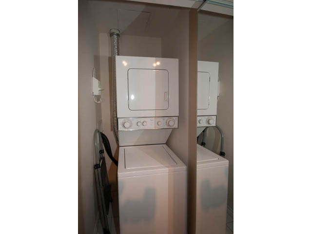 Laundry room with stacked washer and dryer, white walls, and utility hose. - 3405-1111 W Pender, Vancouver Downtown