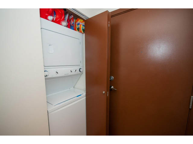 Laundry room with stacked washer and dryer, red detergent bottles visible. - 1702 - 928 Beatty Street, Vancouver Downtown